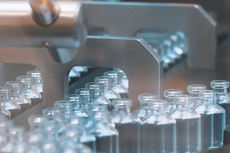 Pharmaceutical production line, crammed with empty glass vials running through a stainless steel machine  