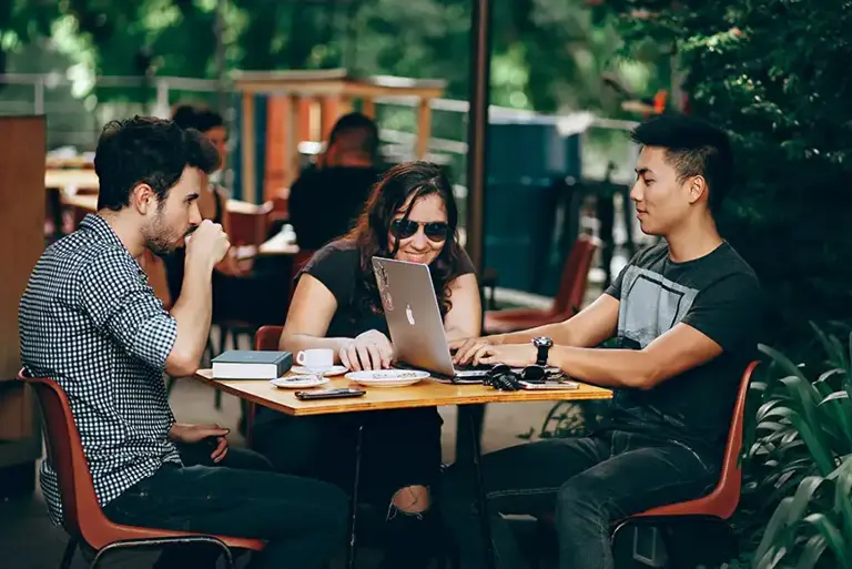 Three young causally dress workers sit working at a small table outside a glass fronted coffee shop