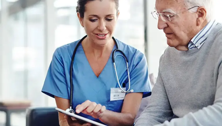 Healthcare professional sits with an older man to explain something on a clipboard