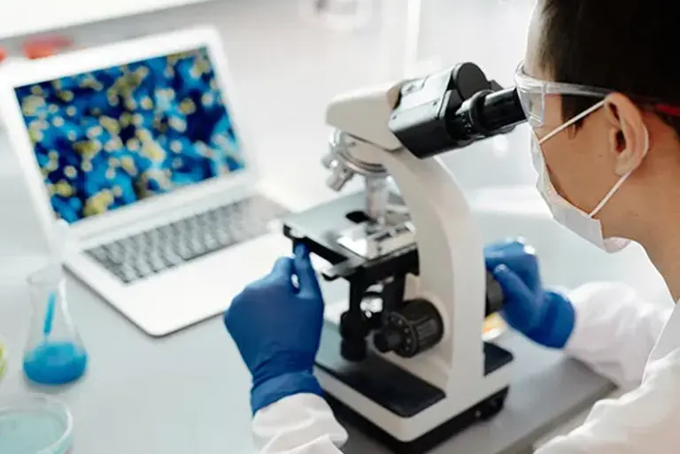 Over the shoulder view of a scientist looking down a microscope