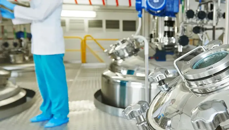 Scientist in the background, with huge stainless steel vats in the foreground 