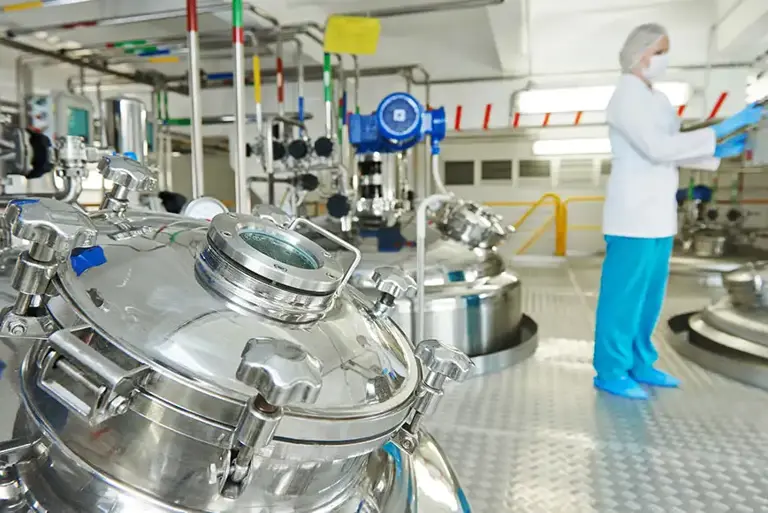 Scientist in the background, with huge stainless steel vats in the foreground 