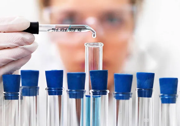 Close up of a rack of test tubes with a scientist adding a single drop from a pipette into the middle test tube.