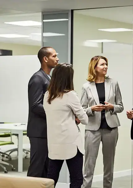 Four office workers stand talking in front of a set of glass meeting rooms