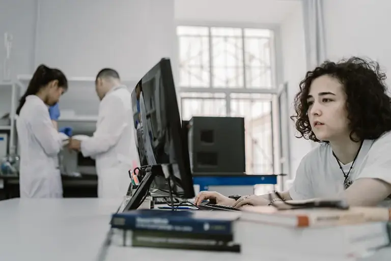 Scientist in the lab looks at a computer screen, while two others talk in the background