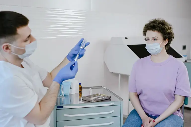 Female patient sits awaiting the the injection being prepared by a healthcare professional