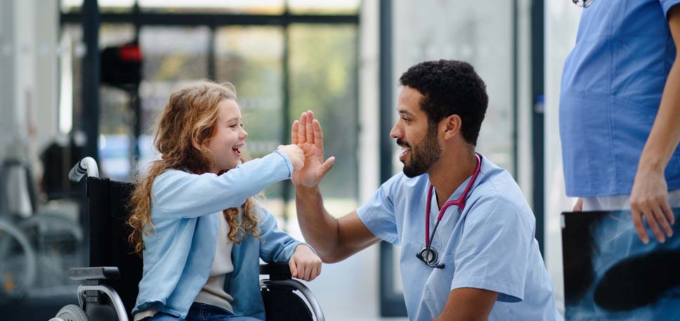 A young girl in a wheelchair enthusiastically high fives a doctor.